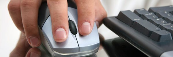 Hand on mouse next to a keyboard in the background.